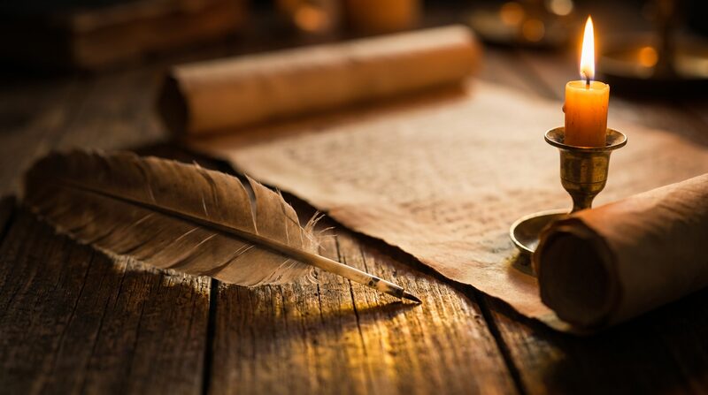 Pluma y pergamino con escritura hebrea bajo luz de vela