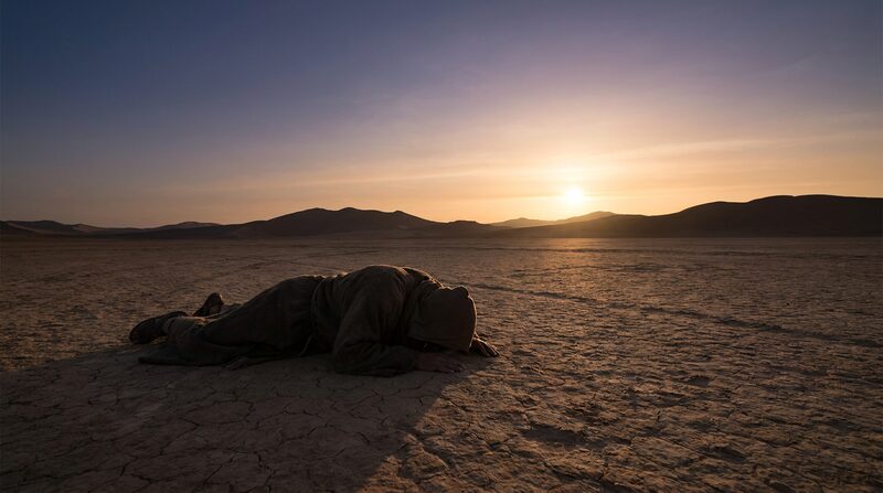 Una figura solitaria postrada en el suelo del desierto al primer rayo del amanecer