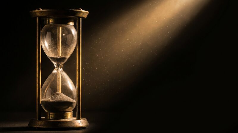 Reloj de arena antiguo casi vacío iluminado por un rayo de luz dorada sobre fondo oscuro